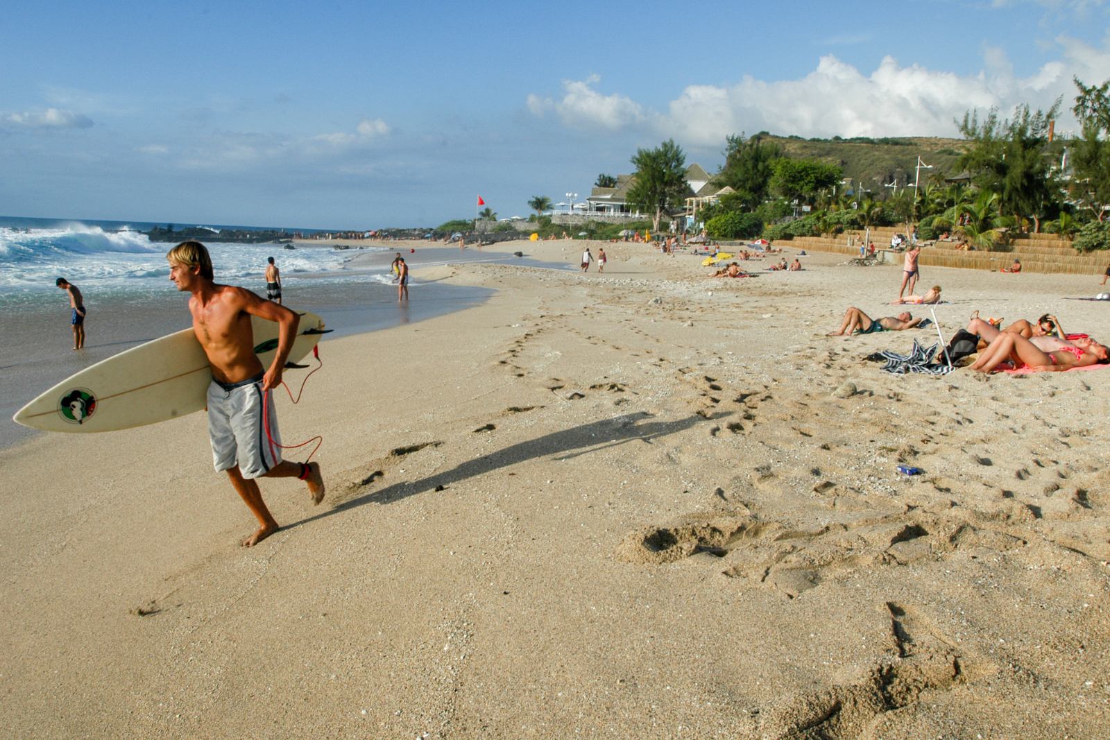 Surf à Boucan Canot, La Réunion Surfer sortant de l’eau à Boucan Canot avec sa planche, plage animée en arrière-plan