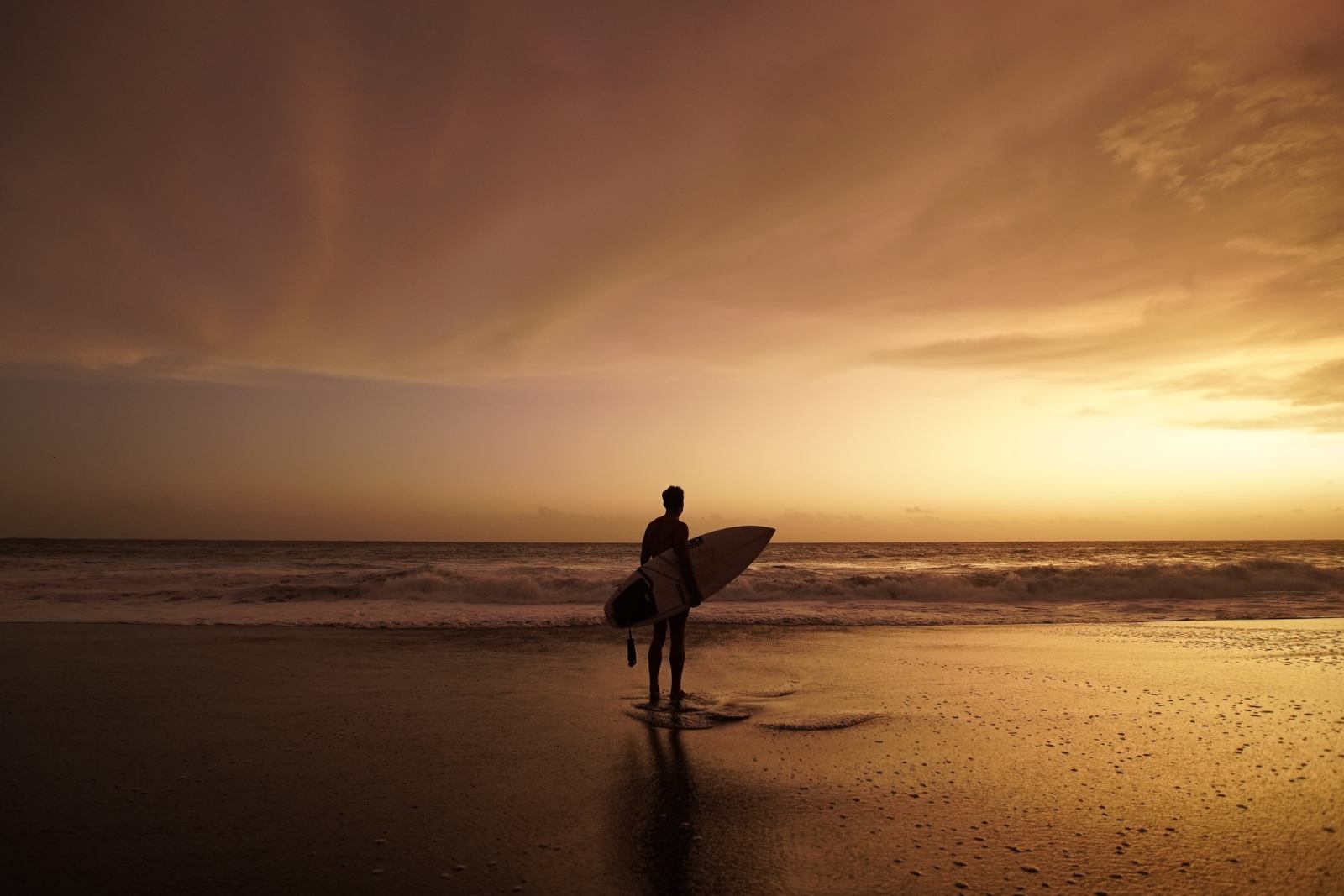 Surfer face aux vagues à La Réunion Surfer de dos observant les vagues au coucher du soleil sur une plage de La Réunion