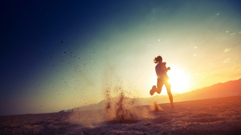 Coureur participant à un trail nocturne à La Réunion, illuminé par un coucher de soleil avec les montagnes en toile de fond