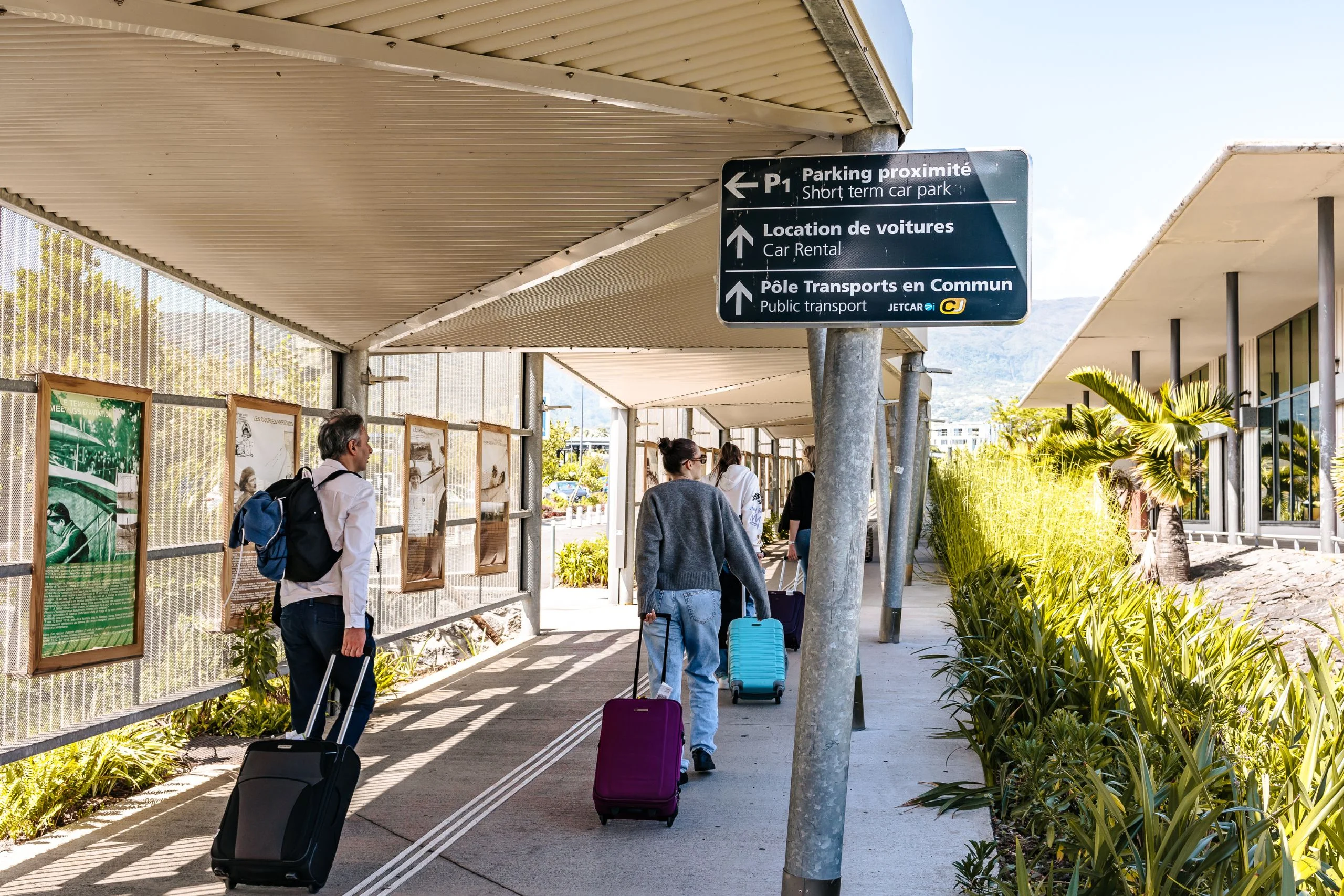 Voyageurs en route vers la zone de location de voitures à l'aéroport Roland Garros La Réunion via la passerelle piétonne